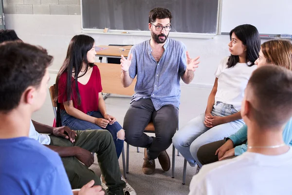 stock image Diverse group of high school students sitting on chairs in a circle and interacting during a lesson, their Caucasian male teacher with them and talking. Education concept. High quality photo