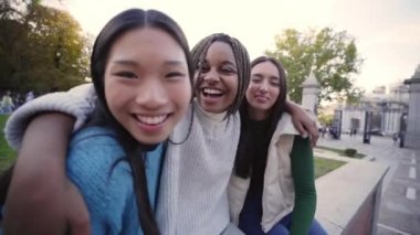 Üç neşeli bayan arkadaştan oluşan bir grup birbirlerine sarılmış kameraya bakıyor. Farklı ırklardan mutlu kızlar arkadaşlığı kutlarken gülüyorlar. Erasmus öğrencileri dışarıda vakit geçiriyorlar.