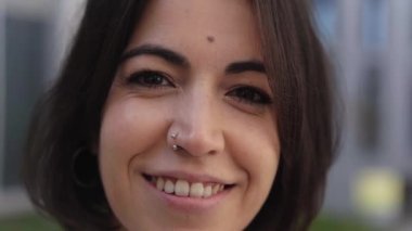 Resmi takım elbiseli gülümseyen Hintli genç bayanın kameraya bakışını yakından çek. Sokaktaki insanlar mutlu bir iş kadını portresi çiziyor. Güzel modern yönetici bir finans merkezi binasında.