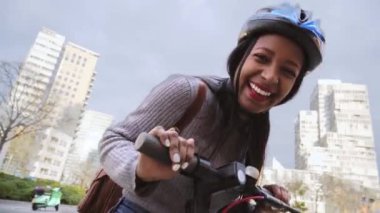 Şehir merkezinde elektrikli scooterla gezen güzel bir kadın. Neşeli Latin kızlar kask takarak gülümser.