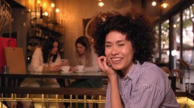 Neşeli bir bar sahibinin uzay portresini kopyala. Latin güçlü kıvırcık saçlı kadın kameraya bakıyor. Kız arkadaşlar barda eğleniyor. Alışverişten sonra üç bayan meslektaşım,