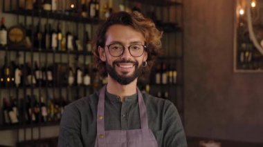 Küçük bir yerel işletmenin genç sahibinin kamera portresine bakıyorum. Neşeli erkek barmen, olumlu bir tavırla gülümsüyor. Neşeli bar işçisi içerde dururken gülümsüyor..