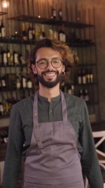 Küçük bir yerel işletmenin genç sahibinin kamera portresine bakıyorum. Neşeli erkek barmen, olumlu bir tavırla gülümsüyor. Neşeli bar işçisi içerde dururken gülümsüyor..