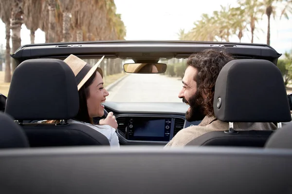 Güneşli bir günde üstü açık bir arabayla birbirlerine bakıp gülümseyen neşeli beyaz bir çift. Bir ülkede turistik şehir seyahati. Şehir manzarası tatilleri mutlu erkek ve kadın eğleniyor