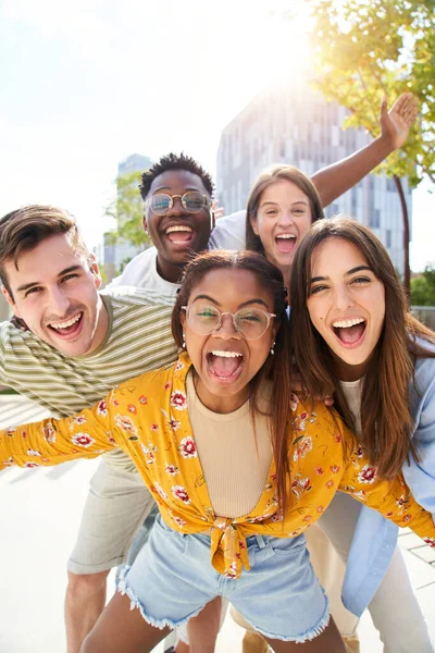 Dikey fotoğraf Mutlu arkadaşlar kameraya bakıyor ve gülüyor. Gülümseyen bir grup insan dışarıda eğleniyor. Öğrenci üniversitesinin neşeli topluluğu. Çok kültürlü insanların yaşam tarzı neşeli..