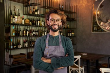 Küçük bir yerel işletmenin Müslüman sahibinin kamera portresine bakıyorum. Neşeli erkek barmen, olumlu bir tavırla gülümsüyor. Neşeli bar işçisi içerde dururken gülümsüyor..