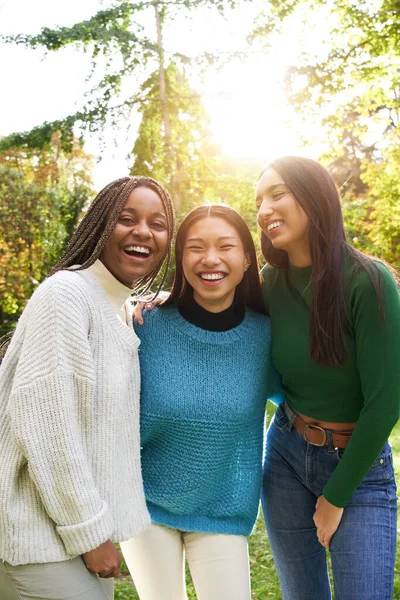 Vertical Portrait of three girls outside looking at the camera. An Asian Chinese woman, black African American and a Caucasian lady together and embracing. Friendship in multi-ethnic groups of people
