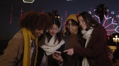 Geceleri elinde cep telefonları olan, kışın giyinmiş, çok ırklı bir grup genç arkadaşın alçak açılı görüntüsü. Gülümseyen insanlar cep telefonu kullanıyor. Teknoloji bağımlılığı çevrimiçi, olumlu insanlar sosyal medya