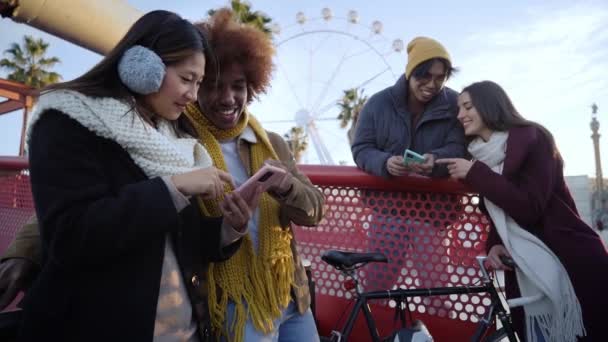 一群年轻的混血种族的人穿着冬装 户外带着手机 兴奋的学生使用他们的技术设备 年轻企业家的概念 移动应用 嬉皮士千年 — 图库视频影像