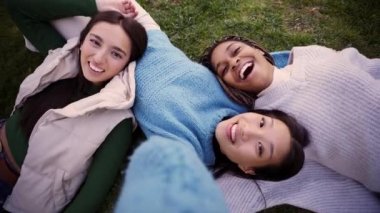 Üç çok ırklı kız çimenlerin üzerinde uzanıp kameraya bakarak selfie çekiyor. Bir grup neşeli arkadaş birlikte eğleniyor, sosyal medyada mutluluğu paylaşıyorlar. Arkadaşlık ve özgürlük kavramı