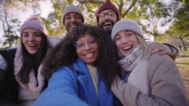 Winter time smiling selfie of a happy group of multicultural friends in video call with phone looking at camera. Cheerful multi-ethnic young diverse people having fun together. Colleague hanging out.