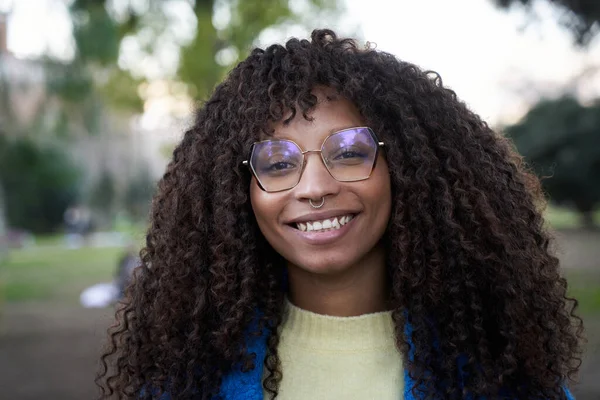 Close up portrait of beautiful smiling young African woman with curly hair looking at camera with positive expression. Happy latin girl wearing eyeglasses outdoors. Cheerful real people.
