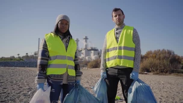 两名年轻的积极分子拿着垃圾袋看着摄像机 一对夫妇站在一起 带着关心的表情 清理志愿者清理自然界中的废物 概念环境护理 — 图库视频影像