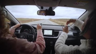 Funny women singing happy while driving automobile. Cool two young girls dancing lively music in car while driving in the countryside. Friends having fun concept. Rear view. Slow motion.