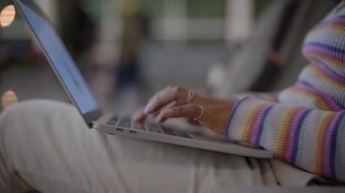 Close-up shot of a young woman typing on a laptop keyboard while sitting at the station. Concept of waiting times. Female using her computer in the airport departure lounge. 