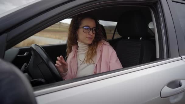 女性が車を起動する シートベルトをしている若い女性 若い女の子が運転席の車の中に座っている カメラが横から撮影している サイドビュー — ストック動画