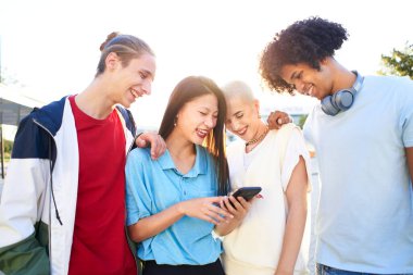 Group o friends watching the smart phone outdoor. Young smiling people sharing with mobile cell outdoors. High quality photo
