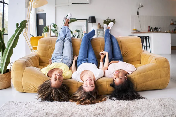 Three mixed race multi ethnic female best friends laugh good happy at sofa home. Cheerful women having fun in amazing loft enjoying life style in living room. Girlfriends affectionate. High quality