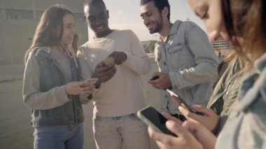 Group of young millennial friends having fun using smartphones and laughing together outdoors. High quality FullHD footage
