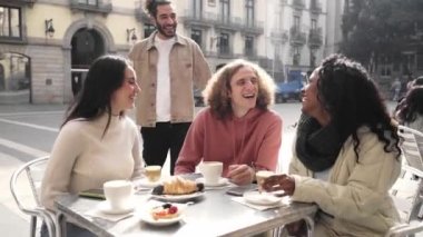 Group of friends meet in the street. People having breakfast outdoors on a terrace on the city street. Man greets his college. High quality photo