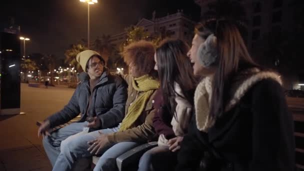 サイドビュー 若い人たちがチャットや夜には通りで笑っている 親友のグループに座って一緒にぶらついている 楽しさと笑顔を持っているカップル 良い時代の概念 — ストック動画