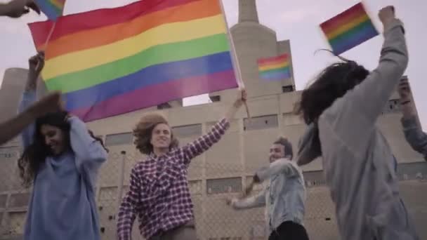 ゲイのパレードで虹の旗を振っている若者のスローモーション ゲイのプライド行進に参加する抗議者のグループ ダンスやお祝い 高品質のフルHd映像 — ストック動画