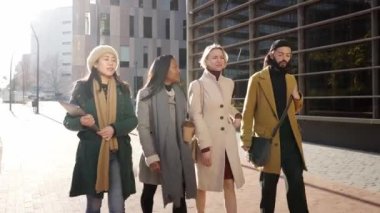 Asian businesswoman and mixed-races people walking outdoor at business center and talking with tablet or laptop device in hands. Multi ethnic work partners discussing project and finance. High quality