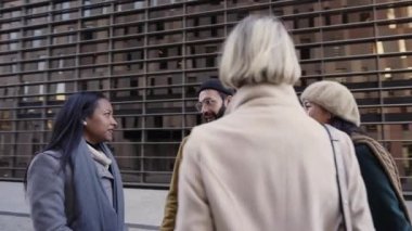 A multi-ethnic group of business people talk happily standing in the middle of the street. Asian woman and African American lady converse with customers on the street near office building. Quality 4k
