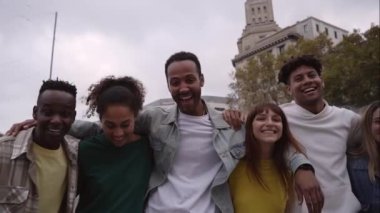 Young people looking camera and walking laughing. Happy friendship mixed race group cheerful together outdoors. Smiling students during a trip. Multi-ethnic colleagues hugging each other in the city.