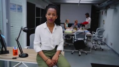Modern ofiste masa başında oturan ciddi bir Afrikalı Amerikalı profesyonel kızın videosu. Şirket toplantısında fotoğraf için poz veren konsantre karışık ırk kadın takım lideri. İşyeri. 