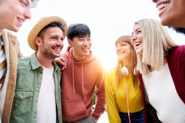 Birbirlerine gülümseyen ve bakan etnik çeşitliliğe sahip bir grup arkadaşın portresi. Uluslararası gençler birlikte vakit geçirmek için dışarıda toplandılar. Erasmus üniversite gezisi.