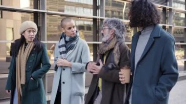 A multi-ethnic group of cheerful business people walking towards outside a corporate center. Middle age manager man explain the plan with the teamwork. High quality 4k footage