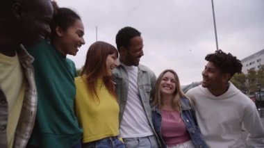 Young group of multiracial friends happy and telling jokes, hugging and laughing loudly outdoors. Concept of tourism, travel, leisure and adolescence. People spending quality time together.