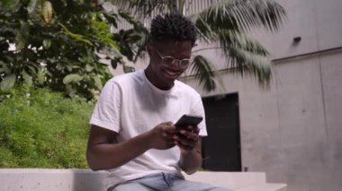 Video of a happy black man using a mobile phone on break from work. Smiling African American man texting and checking social media. Cheerful millennial connecting to an online application.
