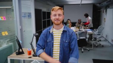 Modern bir ofisteki genç kızıl saçlı programcı ya da iş adamı kameraya bakıp gülümsüyor. Kollarını kavuşturmuş serbest çalışan bir adam toplantı odasında bir video için poz veriyor. İş arkadaşları arka planda çalışır.