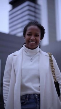 Vertical young African American business woman standing outside business center looking at camera. Smiling confident black lawyer girl poses happily in downtown. Enterprising people posing outdoors.