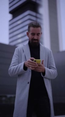 Vertical video of handsome young businessman checks his next meeting on the cell phone outside a business center. Close up portrait of manager thumb up smiling to camera outdoors. Enterprising people.