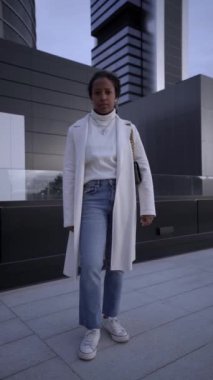 Vertical young African American business woman standing outside business center looking at camera. Confident and serious black entrepreneur girl with arms crossed in downtown. People posing outdoors.