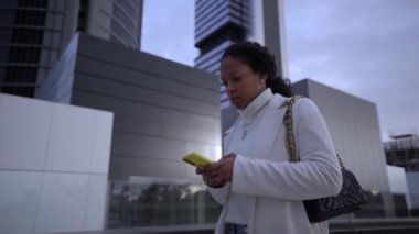 Video of young African American business woman using cell phone on her way to work business center. Confident and serious black girl talking on mobile. Professional people walking outdoors.