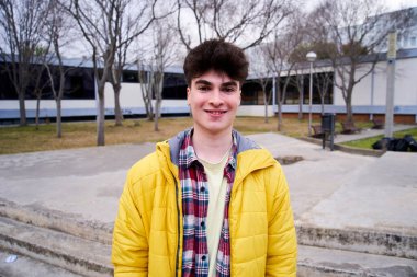 Portrait of a student boy looking at the camera outdoors. College campus lifestyle young people happy smile. Opponent posing for photo before exam. Library courtyard in autumn. 