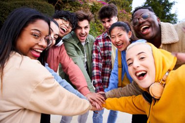 Cheerful multiracial group of students making pile hands and smiling at the camera on campus. Concept celebrating companionship learning and education. Happy people having fun together. International.