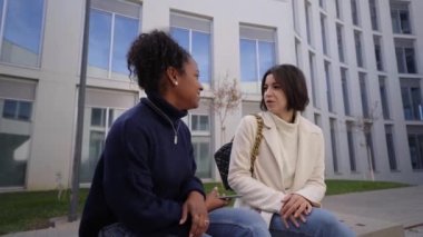 Two young female workers talking business and sitting outside a financial center. Couple of businesswomen coming to an agreement while taking a break. Meeting of empowered women entrepreneurs.