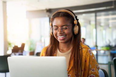 Young black African college girl studying online on her laptop. Smiling applied Latin woman taking an online virtual class sitting in campus cafeteria. Close-up portrait happy woman in concentration.