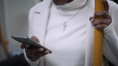 Pretty young African girl standing using cell phone in subway. Beautiful happy black woman consulting phone on transport. Cosmopolitan people moving around the city. 