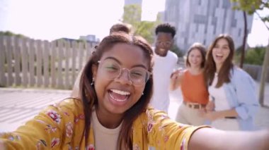 Mutlu genç arkadaşlar kutlama ve zıplama videoları çekiyorlar. Gülümseyen bir grup insan dışarıda birlikte eğleniyor. Selfie çeken devlet üniversitesi öğrencileri. Hayat tarzı neşeli, çok kültürlü insanlar..