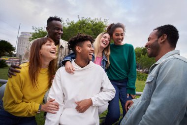 Young group of cheerful multiracial friends looking at each other and laughing outdoors. Concept of tourism, travel, leisure and adolescence. People spending time together in the city park.