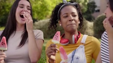 Close up faces three smiling young multi-ethnic women outdoors eating ice cream. Friends having a fun conversation and enjoying the summer atmosphere together. Vacation time. Concept of friendship.
