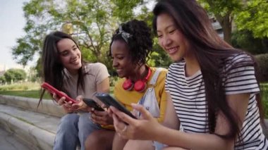Dışarıda cep telefonu kullanan mutlu genç kadınlar. Grup gülümsemesi üniversite arkadaşları akıllı telefondan sosyal ağları kontrol ediyorlar. Sınıf arkadaşları cep telefonunda flört uygulamalarını izlerken eğleniyorlar. Genç kızlar internette flört ediyor.. 