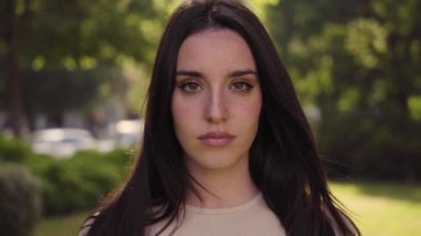 Close up young serious woman looking camera. Attractive female standing on street city lifestyle. Beautiful girl outdoors. Concentrated lady emotional expression on urban background. Empowered people.