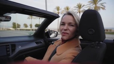 Video beautiful elegant mature woman smile in convertible car. Beautiful lady making peace sign and touching her hair. People renting car for holiday vacation. Funny moments outdoors.